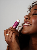 A woman with curly hair is smiling and holding a purple lip balm in her hand.