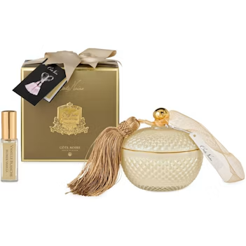 a set of luxury items, including a gold-colored box, a small white glass jar with a gold tassel, and a small gold-colored bottle.