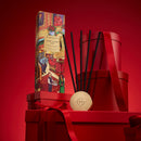 a red box with a picture of a man and a woman, along with the text "Gossie House" and "Night Before Christmas" on it, placed on top of a stack of red boxes and a wooden box with a red ribbon.