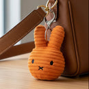 An orange plush bunny charm is hanging from a leather strap of a handbag.