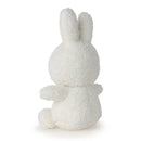 A white, fluffy stuffed bunny toy is sitting on its back with its arms outstretched.