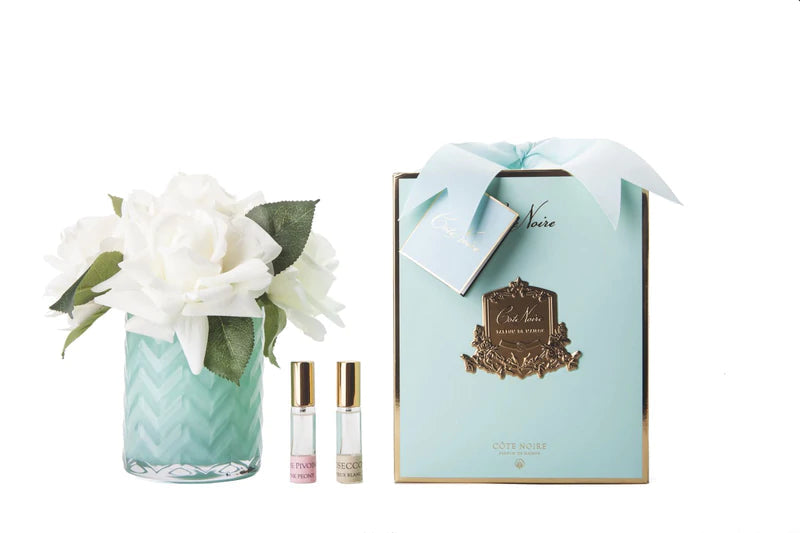 a bouquet of white roses in a glass vase, a box of Cote Noire perfume, and two small bottles of perfume.