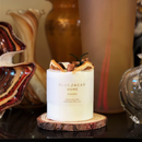 a white candle with text on it, placed on a wooden coaster, surrounded by various decorative items.