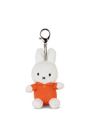 A small white stuffed bunny wearing an orange shirt and sitting on a white surface.