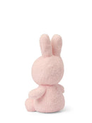 A pink stuffed bunny toy is sitting on its back with its ears perked up, facing away from the camera.