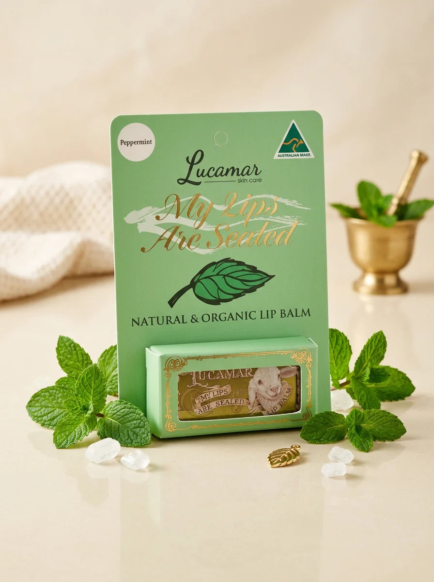A green box of Lucamar My Lips Are Seeded lip balm, surrounded by fresh mint leaves and a small gold bowl with a spoon.