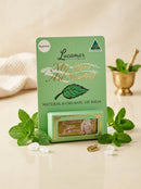 A green box of Lucamar My Lips Are Seeded lip balm, surrounded by fresh mint leaves and a small gold bowl with a spoon.