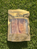 A package of dried meat, specifically "LING MAW", is lying on the grass.