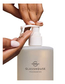 A person's hands applying a liquid product from a pump bottle labeled "GLASSHOUSE FRAGRANCES".