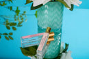 a vase with white flowers and a bottle of perfume placed on a blue surface.