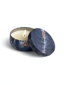 A blue and white patterned tin candle holder with a lit candle inside, placed on a white surface.
