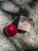 a red lip balm and a box of Kakadu Plum moisturizing lip balm, both placed on a textured surface.