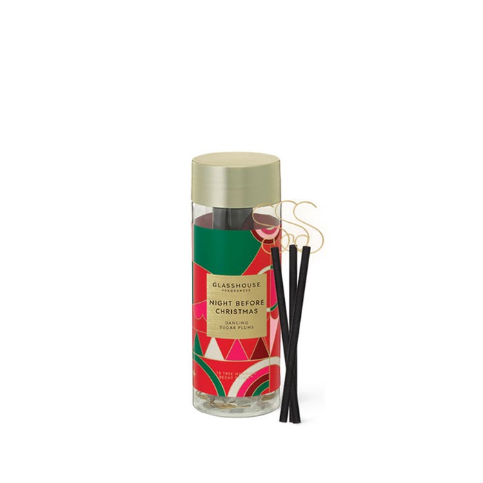 A cylindrical glass jar with a gold lid, containing black incense sticks, and a label that reads "GLASSHOUSE" and "NIGHT BEFORE CHRISTMAS"