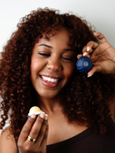 A woman with curly hair is smiling and holding a blue and yellow round object in her hand.