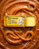 a yellow tin of Lucamar lip balm surrounded by caramel sauce and sprinkled with sea salt.