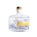 A clear glass bottle with a gold cap, containing a transparent liquid and decorated with purple flowers. The bottle has a yellow label that reads "BLUEOCAR HOME Fragrance Diffuser".