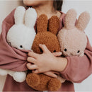 A child is holding three stuffed rabbits in their arms, wearing a pink sweater.