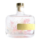 A clear glass bottle with a gold label that contains pink flowers and the text "BLUEJACAR HOME Fragrance Diffuser".