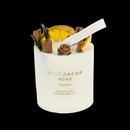 A cylindrical candle labeled "Blue Jacar Home Australia" with dried flower and pine cone decorations on top, set against a black background.