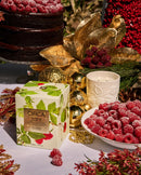 a table with a variety of items, including a box of CIRCA raspberry-flavored tea, a bowl of raspberries, a candle, and a cake. The table is decorated with gold and red ornaments, and the overall scene appears to be a festive or holiday-themed setting.