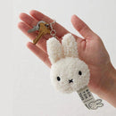 A hand holding a keychain with a white stuffed bunny head and a key attached to it.