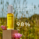 A bottle of "Jurique" face oil, specifically "RARE ROSE FACE OIL", is shown against a blurred background of a field with flowers. The text highlights the oil as a "next-generation face oil" that is "perfect for dehydrated skin, for more supply, smoother skin." The image also states that the oil is " Clinically proven to instantly strengthen skin barrier function in 98% of participants."
