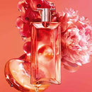 A perfume bottle with a red and orange color scheme is surrounded by a pink flower and a slice of orange, creating a visually appealing and vibrant composition.