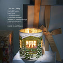 A candle in a white container with a winter scene design, placed on a table with a striped ribbon.