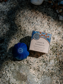 A blue lip balm and a box of lip balm are placed on a stone surface, with the text "KoH Lemon & Eucalyptus Moisturizing lip balm Australian Made" visible.