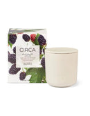 a white ceramic candle holder with a lid, placed next to a box of blackberry and plum-scented soy candles.