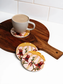 A wooden serving board holds a white mug filled with a beverage, accompanied by two coasters with a floral design.