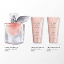 a collection of three beauty products from the brand "La Vie est Belle". The products include a perfume bottle, a shower gel bottle, and a body lotion bottle.