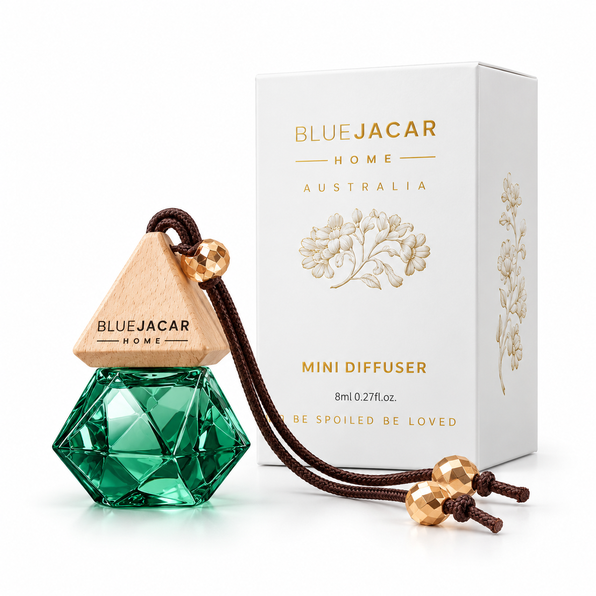 a BLUEJACAR HOME AUSTRALIA MINI DIFFUSER DEITIES OF THE SUN AND FLOWERS diffuser, which is a green crystal-like bottle with a brown string attached to it. The diffuser is placed next to its packaging box, which is white and has gold text and graphics on it.