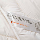 a close-up view of a white fabric, possibly a blanket or quilt, with a label that reads "MINJUMBUK THERMAL WOOL QUILT".