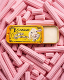A tin of pink lip balm with a picture of a lamb on it, surrounded by pink lip balm sticks.