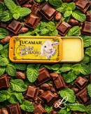 a tin of Lucamar lip balm surrounded by chocolate pieces and mint leaves.