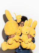 A young child is holding a large yellow stuffed rabbit in front of them, with several smaller stuffed rabbits also present.