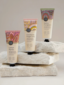 Three tubes of hand cream with different scents and colors are displayed on a stack of white rocks.