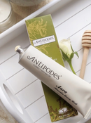 a tube of Antipodes' Honey Mask and a box of the product, along with a honey dipper and a white rose.