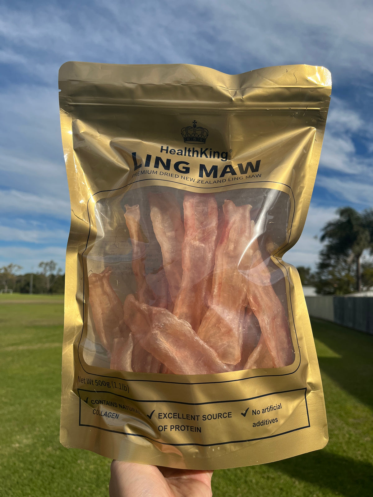 A hand holding a package of bacon strips against a blue sky background.
