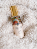 A bottle of "Native Frangipani & Peach Blossom" perfume with a gold cap, placed on a fluffy white surface.