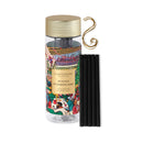 A clear glass bottle with a gold cap, containing a colorful illustration of a winter wonderland scene, along with a set of black sticks.