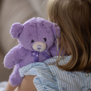 A young girl is holding a purple teddy bear with a blue ribbon around its neck.