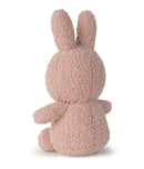 A pink, furry stuffed bunny toy is sitting on its back with its arms and legs spread out.