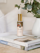 A bottle of "Native Franciscan & Peach Blossom" perfume is placed on top of a stack of books, with a potted plant visible in the background.