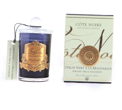 a blue glass candle with a gold label and a white box with a gold label, both of which are labeled as "Côte Noire" and "Citron Vert a la Mandarine".