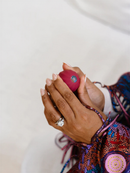 A close-up image of a person's hands holding a red object, possibly a small electronic device or toy, with a ring visible on one of the fingers.