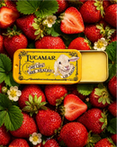 a tin of Lucamar lip balm surrounded by fresh strawberries and leaves.