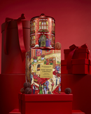 a red gift box with a picture of a building and people, along with the text "GLASSHOUSE NIGHT BEFORE CHRISTMAS DANDELION" and "DANDELION SUGAR FREE". The box is placed on top of a stack of red gift boxes, and there are also some small red balls around the box.